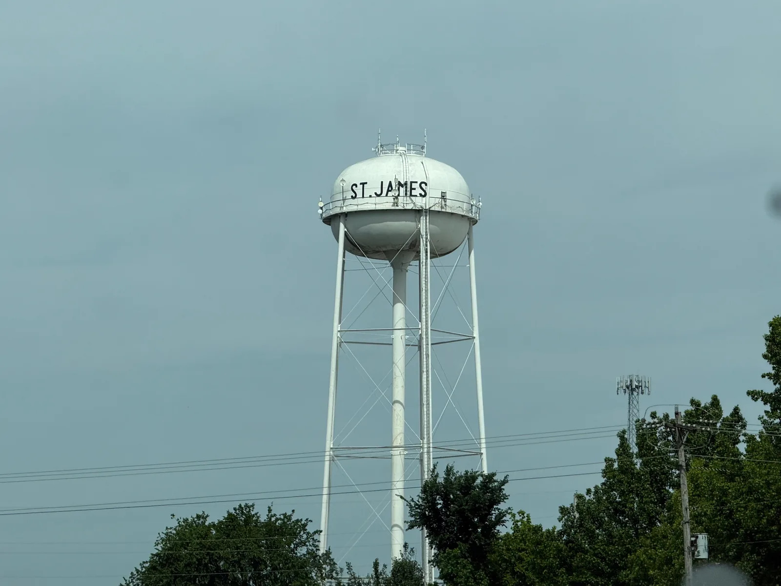 The St. James, Missouri water tower standing tall over green roadside trees along I-44 under an overcast spring sky