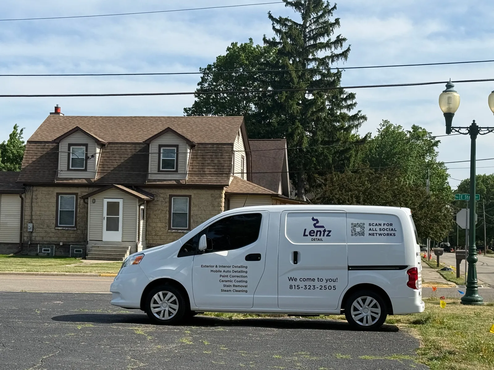 The Lentz Detail mobile detailing van, a white cargo van lettered with their services and the phone number 815-323-2505, parked on a residential street
