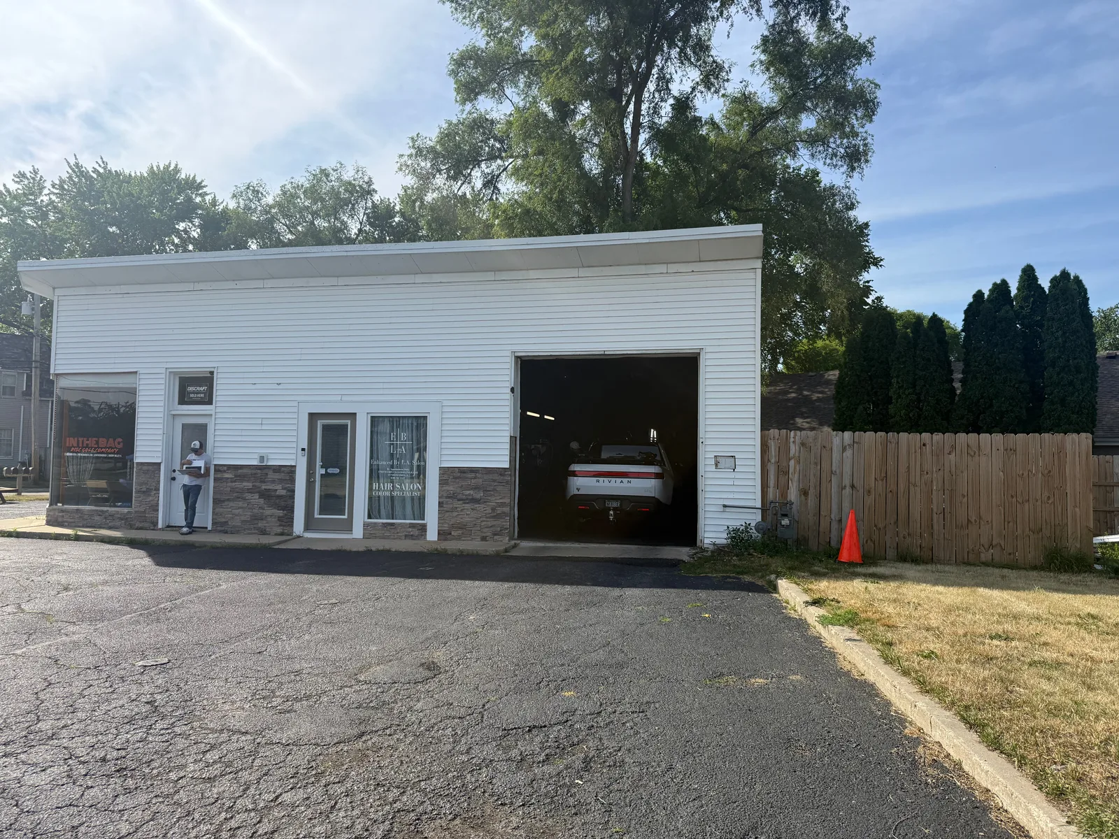 The white Rivian R1T pulled into the open bay of the Lentz Detail shop in Cherry Valley, Illinois, a small white detailing garage with a person standing by the office door