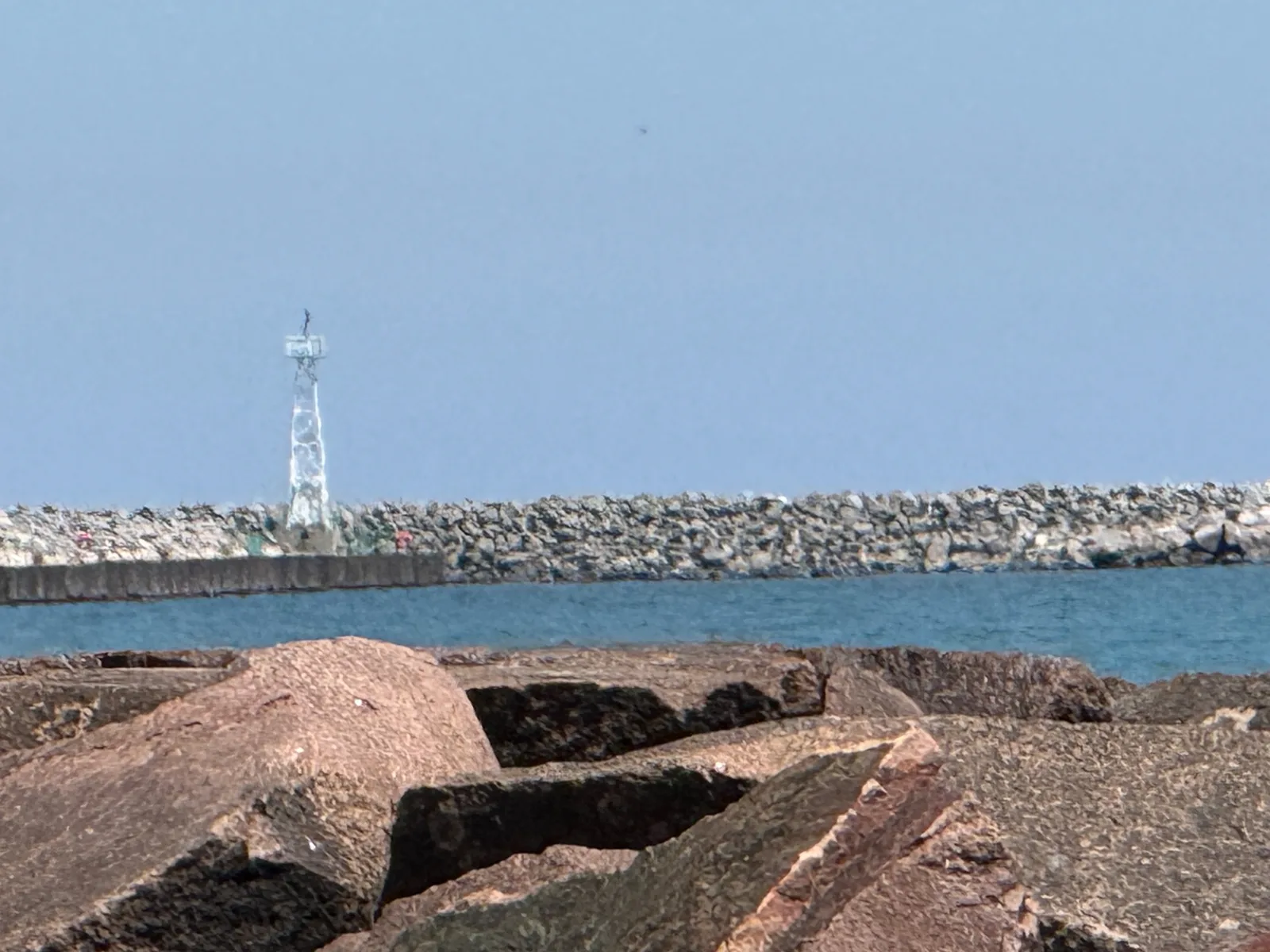 The Racine harbor breakwater and a small white beacon light tower reaching out across Lake Michigan under a clear sky, rocky riprap in the foreground