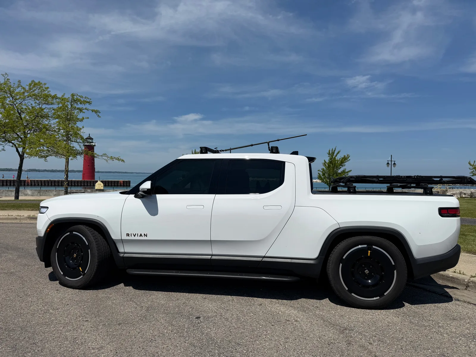 The white Rivian R1T parked at the Kenosha lakefront with the red North Pier pierhead lighthouse and Lake Michigan in the background