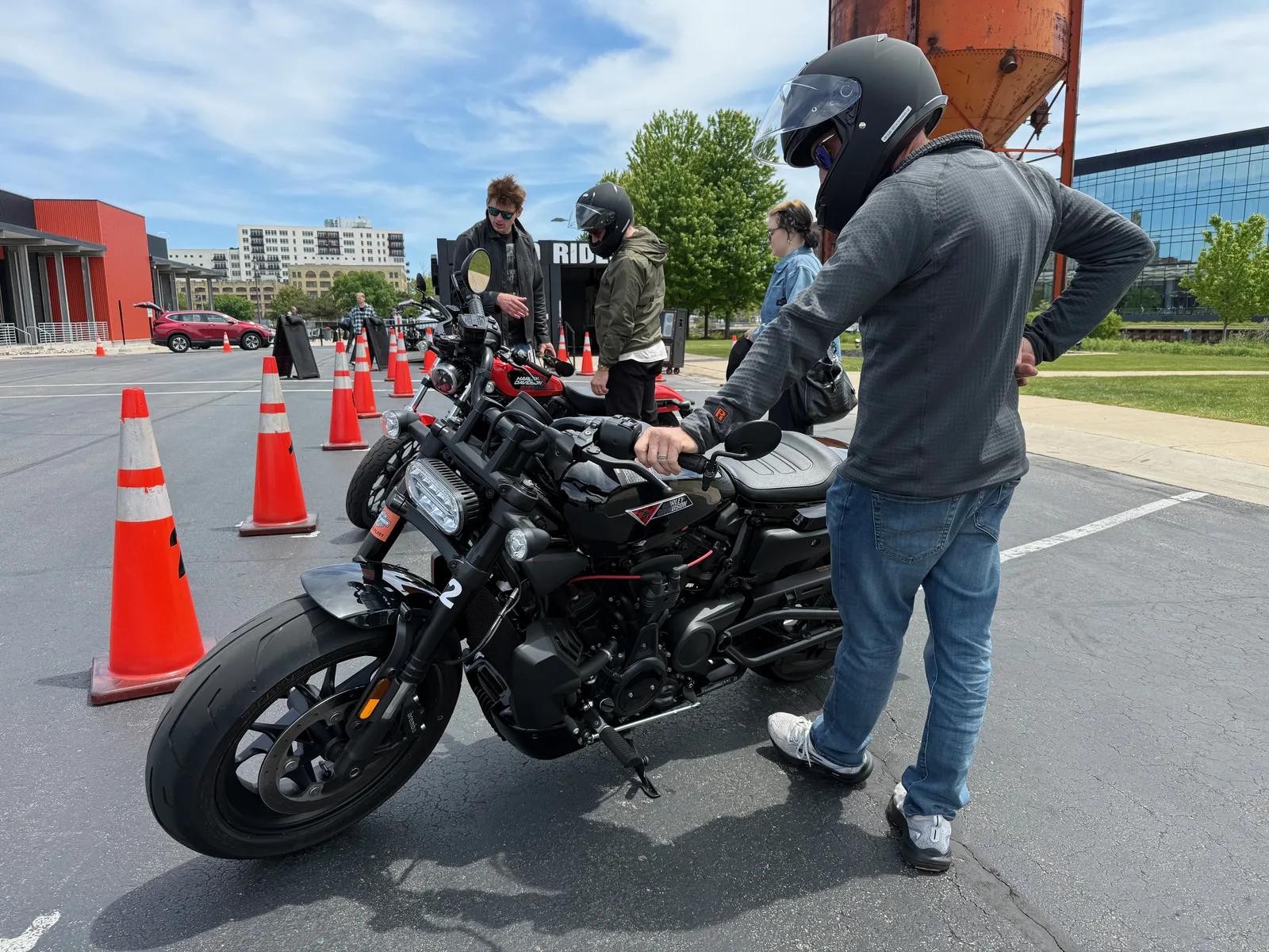 A Harley-Davidson demo rider in a helmet riding through the cone-lined course in downtown Milwaukee under a bright sky