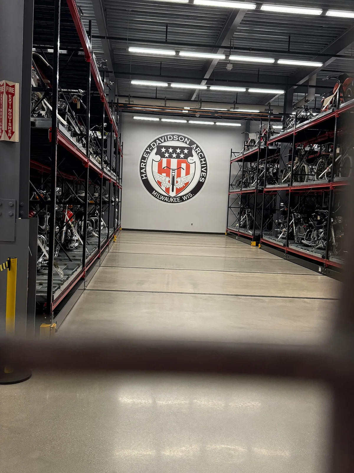 The Harley-Davidson Archives in Milwaukee, aisles of motorcycles racked floor to ceiling on red steel shelving behind the round Harley-Davidson Archives seal