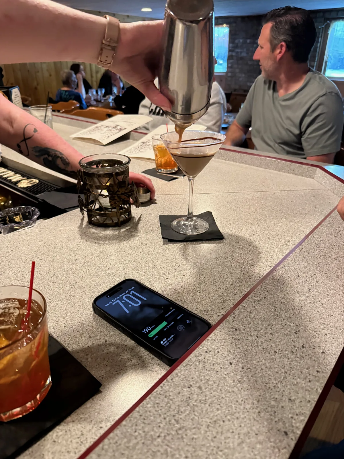 A bartender pouring a freshly shaken espresso martini into a glass at the terrazzo bar at Colony House, an old fashioned and a friend at the bar nearby