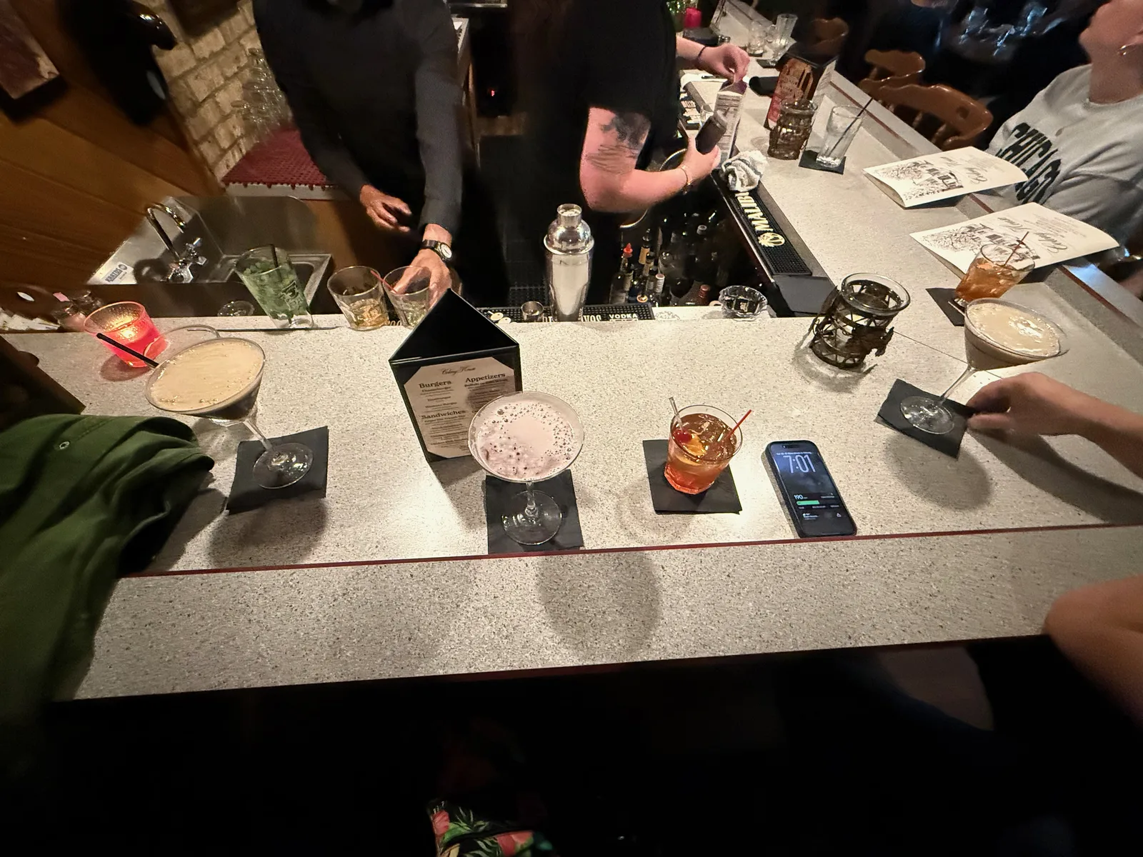 A flight of craft cocktails lined up on a terrazzo bar at the Colony House supper club, an espresso martini and an old fashioned among them, a bartender mixing behind