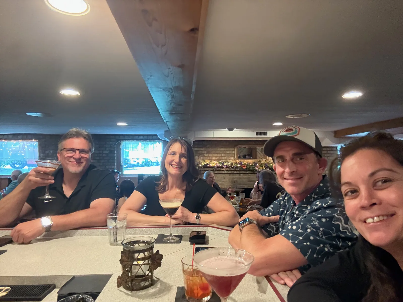 Four friends smiling at the wood-paneled bar at Colony House supper club, cocktails in front of them under warm light