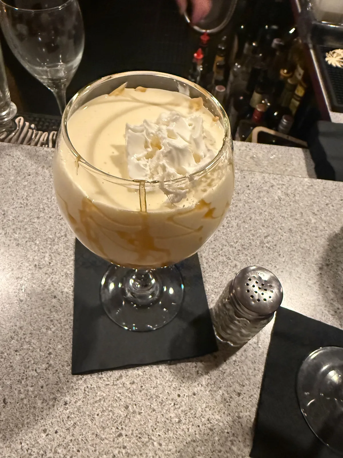 A creamy caramel dessert cocktail topped with whipped cream and caramel drizzle in a stemmed glass on the bar at Colony House