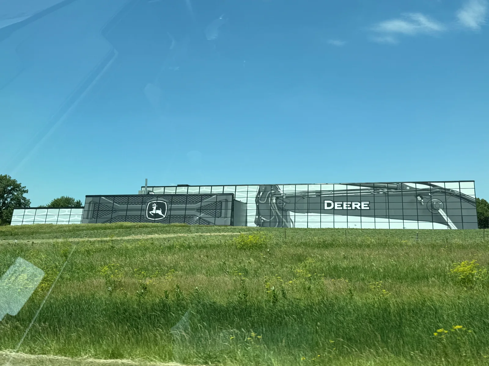 A long glass-fronted John Deere building seen from I-80, the green leaping-deer logo and "DEERE" lettering large on the facade with a combine etched across the windows