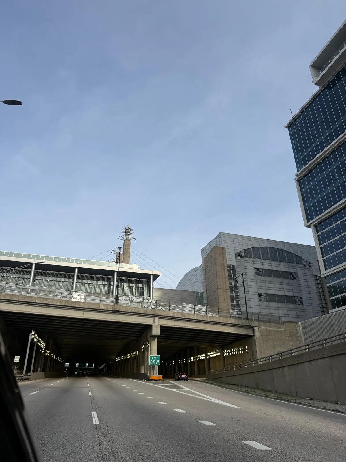 The downtown Kansas City skyline through the windshield from I-70, a green UMKC Health Sciences Campus exit sign overhead