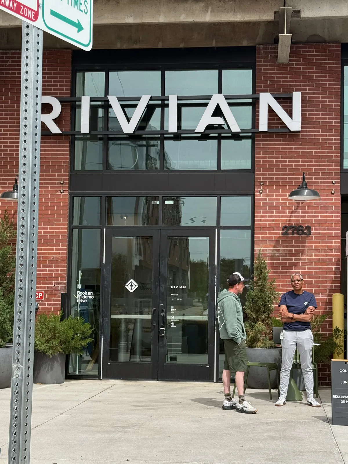 The brick storefront of the Rivian Space in Cherry Creek, Denver, the RIVIAN name mounted above the entrance and a couple standing out front