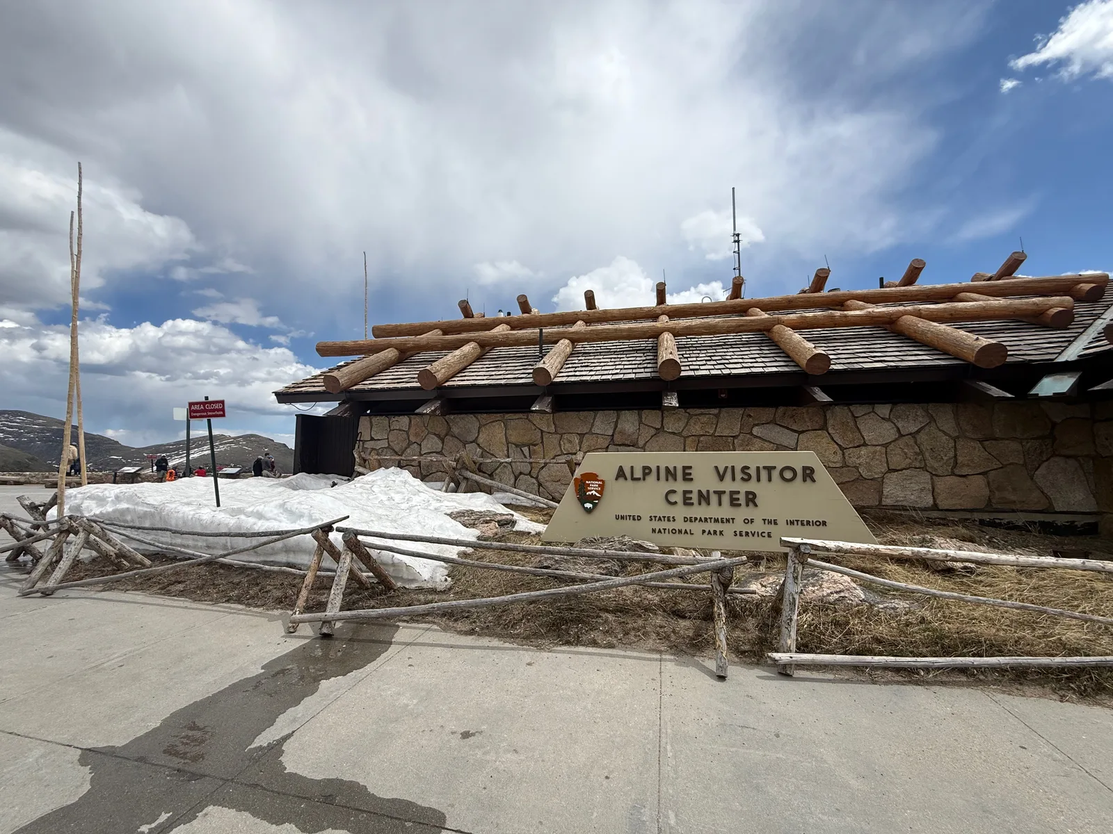 The log-and-stone Alpine Visitor Center at 11,796 feet in Rocky Mountain National Park, the National Park Service sign out front and snow still banked against the building