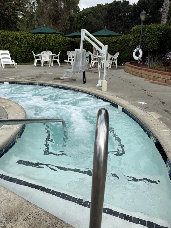 The bubbling hot tub at Campland on the Bay in San Diego, white loungers and green umbrellas on the pool deck behind it