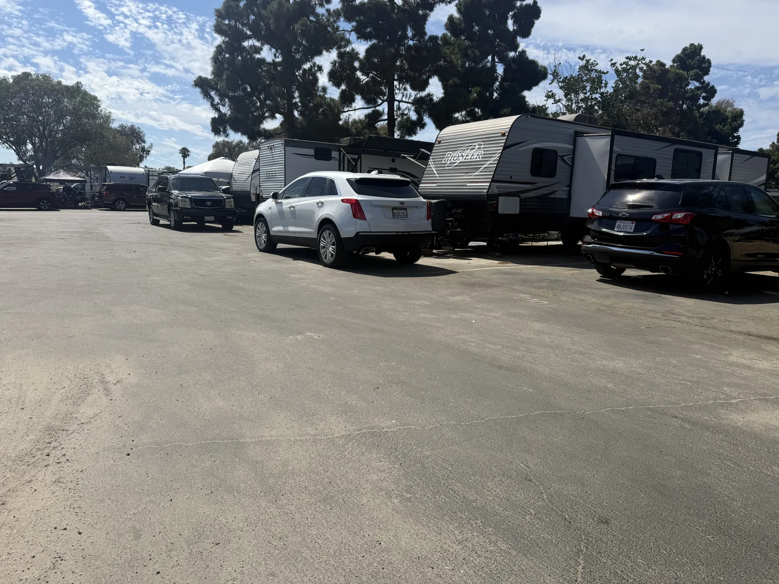 Travel trailers and cars parked close together along an asphalt row at Campland on the Bay, the sites packed in tight under scattered trees