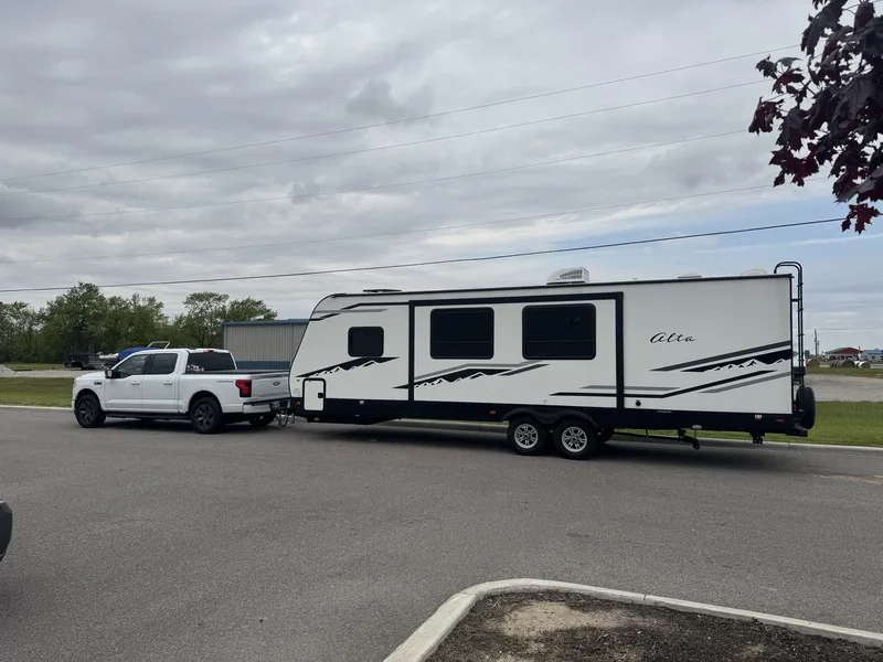 The 32-foot East to West Alta behind the white Ford F-150 Lightning parked on pavement on an overcast travel day.