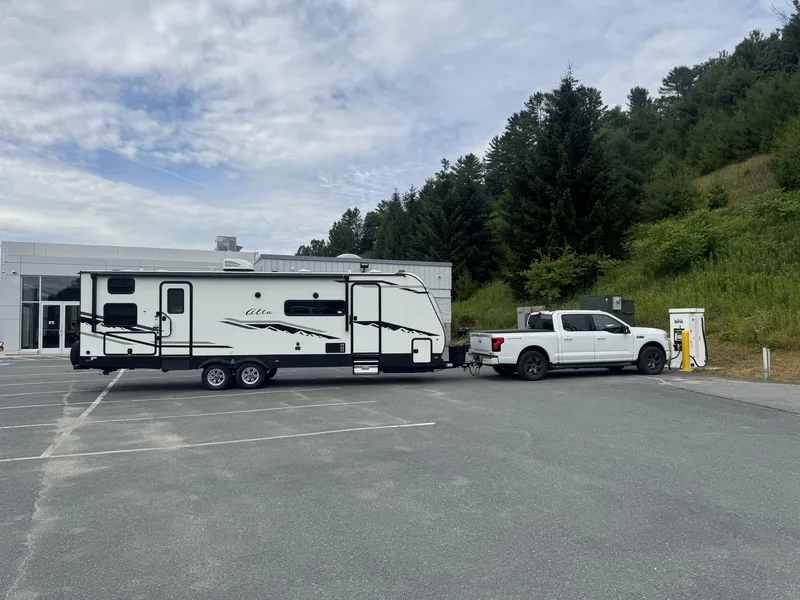 The Ford F-150 Lightning and East to West Alta charging at a Blink station tucked against a green hillside.