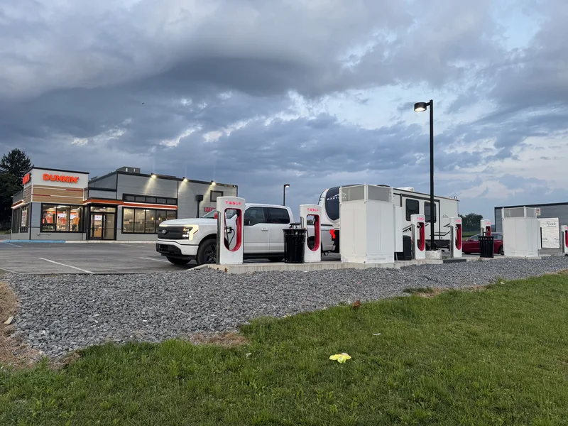 The Ford F-150 Lightning at a Tesla Supercharger beside a Dunkin as a storm front rolls in overhead.