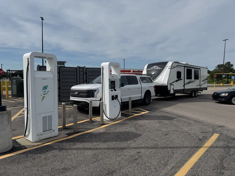 The Ford F-150 Lightning and East to West Alta at a DC fast-charging stop on a bright day, trailer attached.