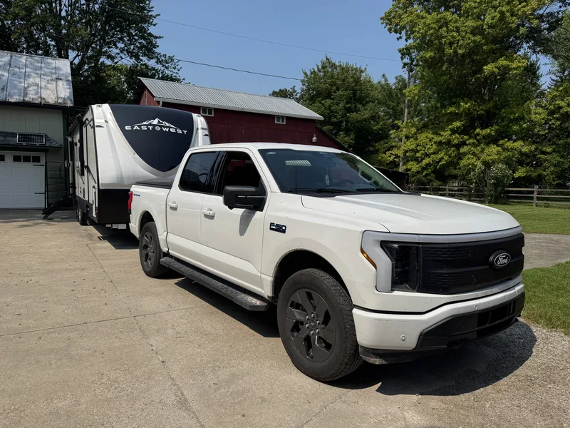 The Ford F-150 Lightning with a bed topper hitched to the East to West Alta in the driveway on a bright morning.