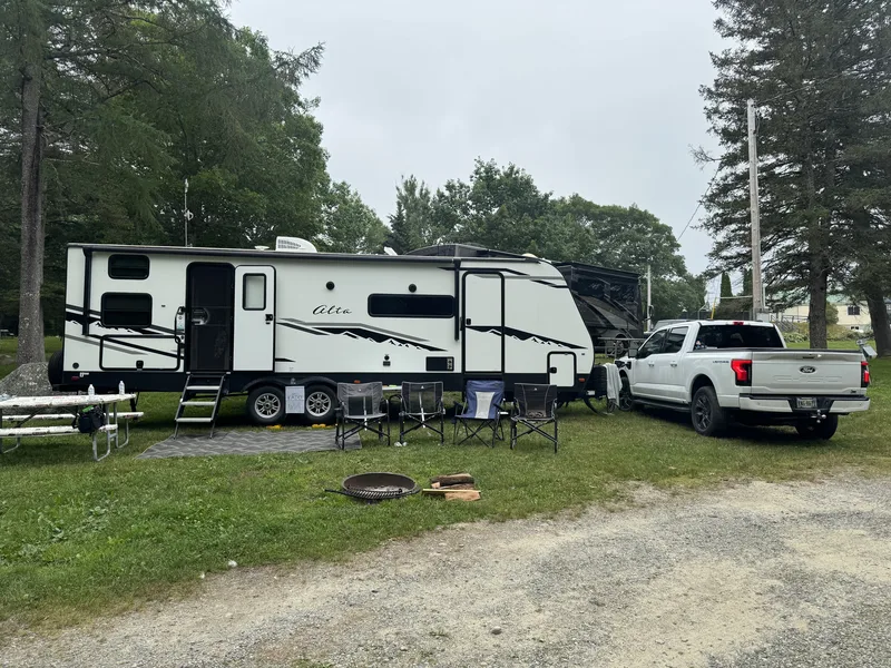 An overcast afternoon at a grassy campsite, camp chairs and a fire ring out, the East to West Alta and Ford F-150 Lightning behind.