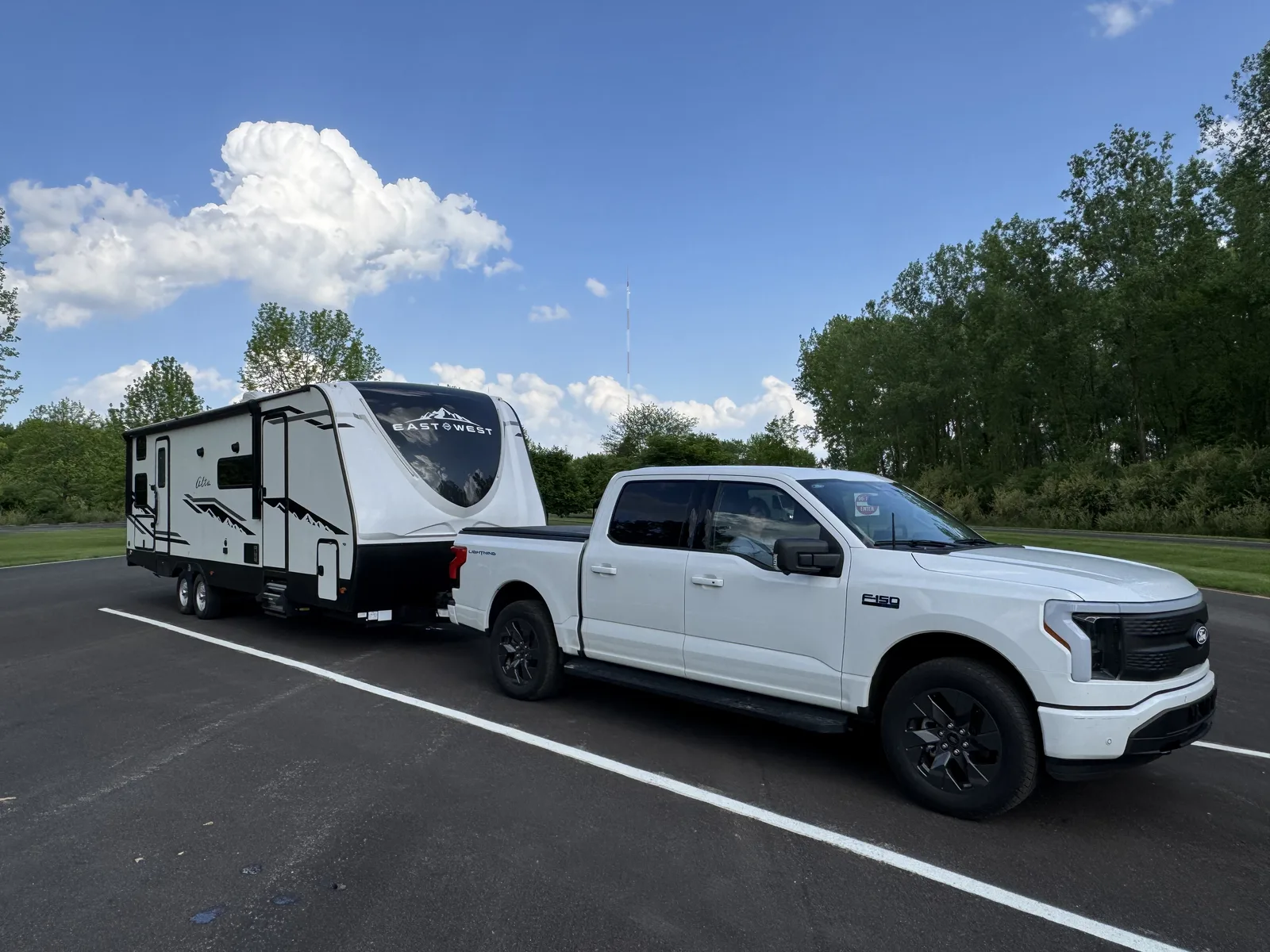 A white Ford F-150 Lightning hitched to a 32-foot East to West Alta travel trailer, parked under a bright blue sky