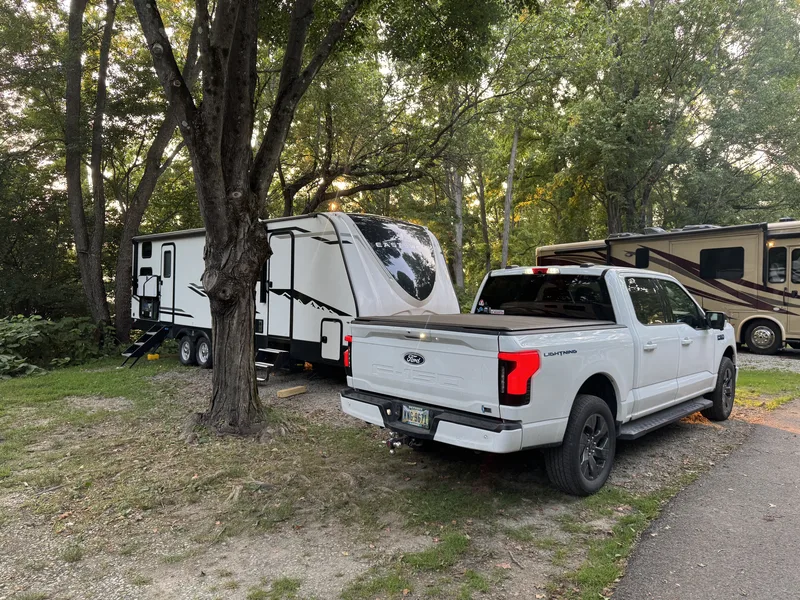 The Ford F-150 Lightning backed into a shaded campsite under large trees beside the East to West Alta.