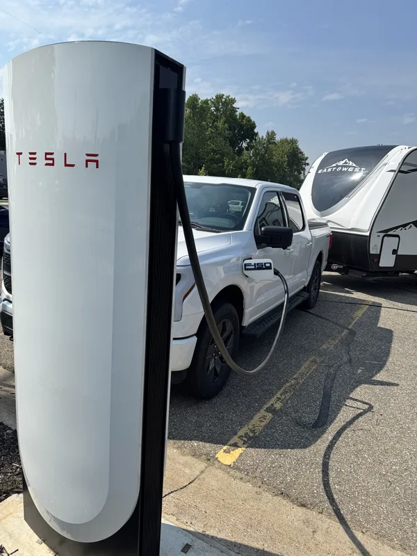 Close-up of the Ford F-150 badge as the Lightning charges at a Tesla Supercharger, the East to West trailer behind.