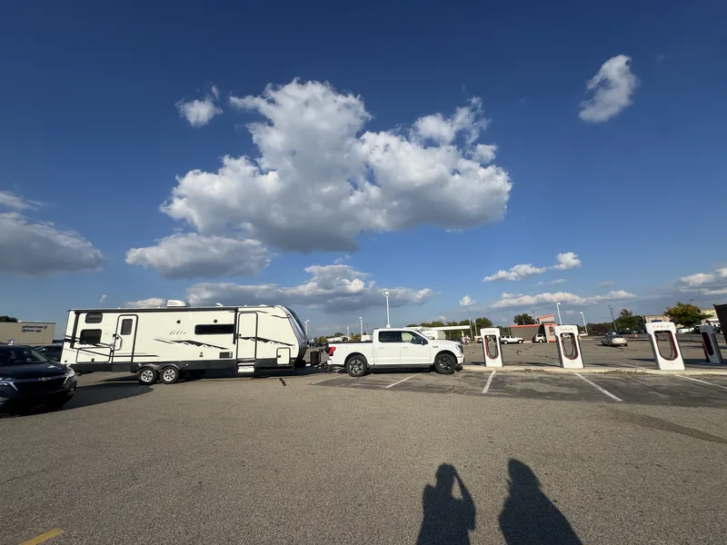 The Ford F-150 Lightning and East to West Alta beside a Tesla Supercharger under big summer clouds.