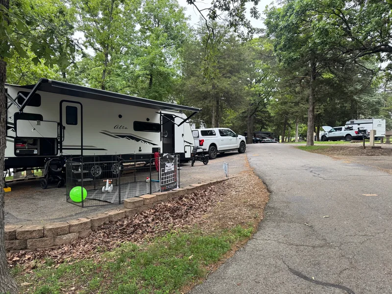 A Ford F-150 Lightning and travel trailer set up at a wooded Branson campsite, plugged into the campground hookup.