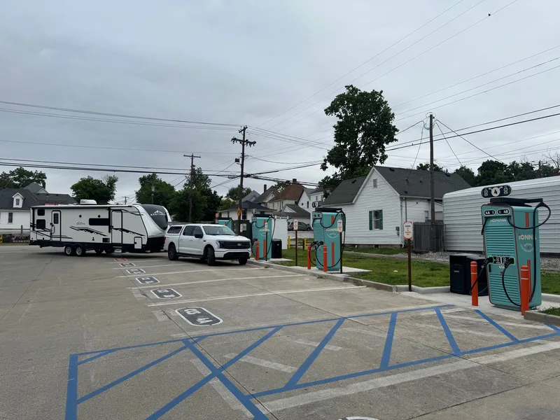 A white Ford F-150 Lightning and travel trailer parked at an IONNA fast-charging station.