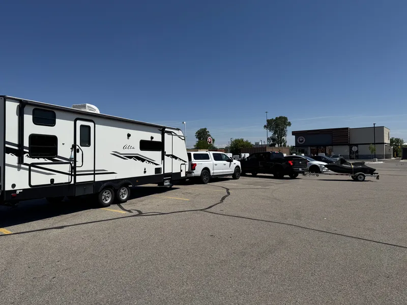The white Ford F-150 Lightning and 32-foot East to West Alta trailer parked at a travel stop, another truck and boat trailer nearby.