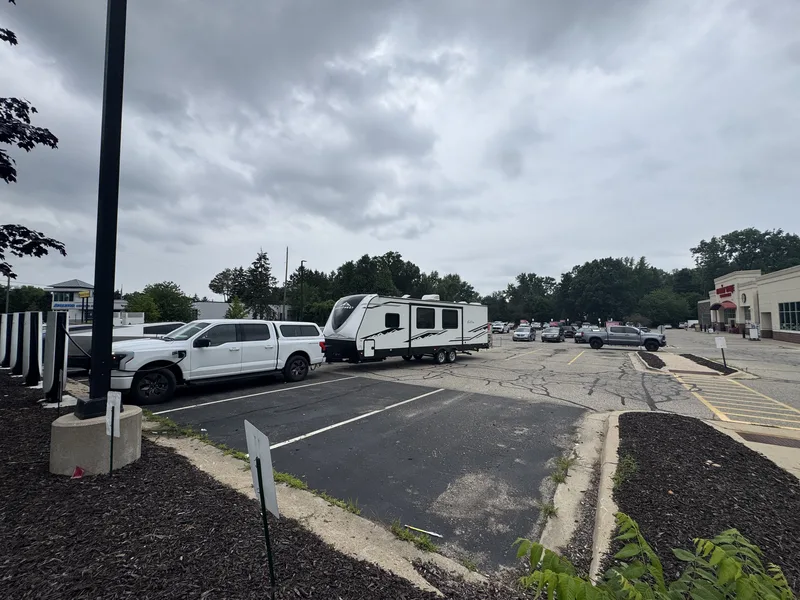 The white Ford F-150 Lightning with a bed topper towing the East to West Alta through a small-town parking lot on a cloudy day.