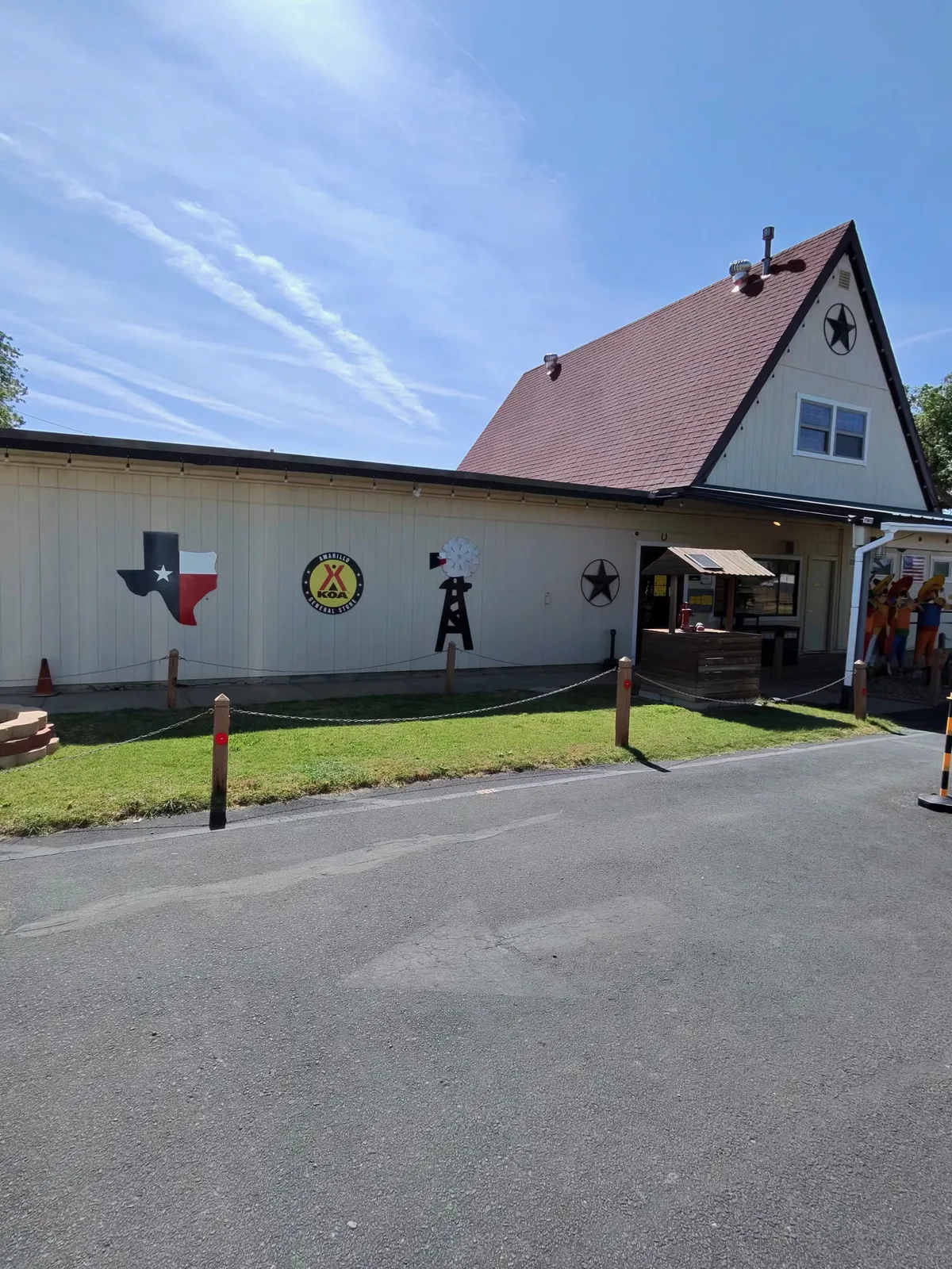 Wider exterior of the Amarillo KOA office and entrance, Texas-themed wall art including a Texas state silhouette, KOA emblem, windmill, oil derrick, and lone star on a white siding wall