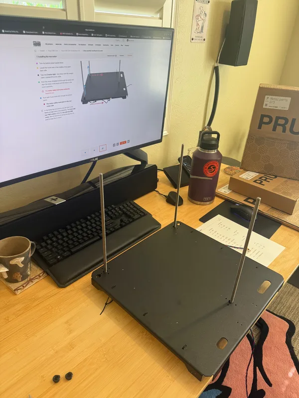 The half-built 3D printer on the bench beside the setup monitor